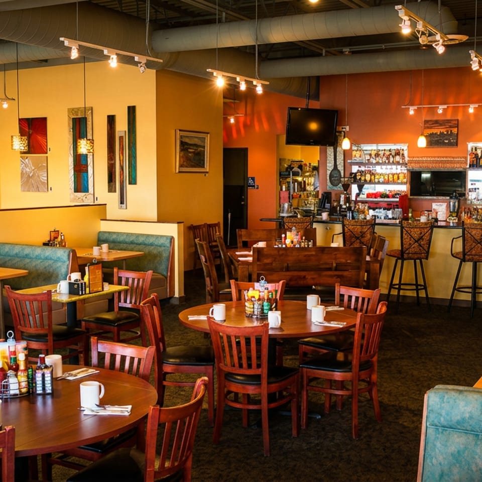 Warmly lit restaurant dining room featuring wooden tables, blue booths, and a full bar.