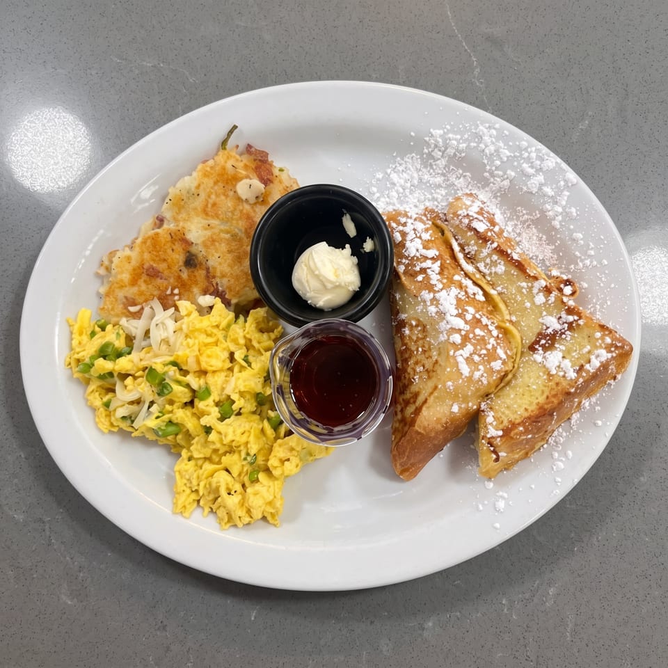 A breakfast plate with scrambled eggs, hash browns, French toast, butter, and syrup.